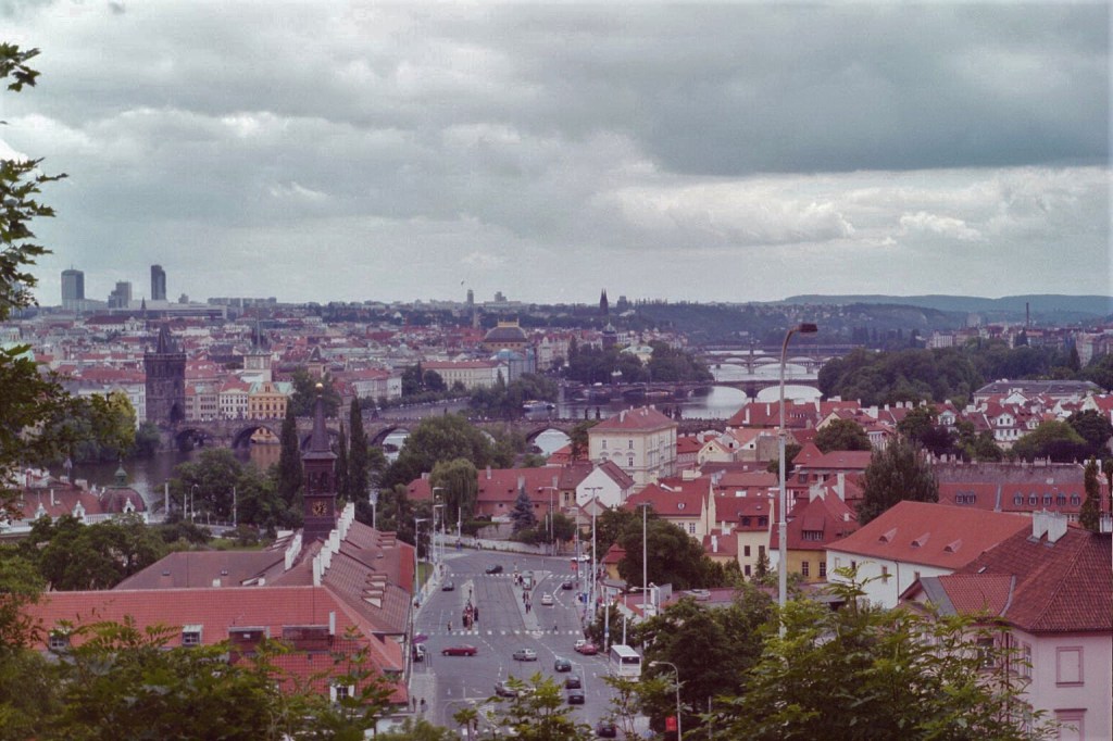 Photograph taken from Prague Castle (Pražský hrad) toward Charles Bridge (Karlův most) and the Vltava River on a cloudy day.