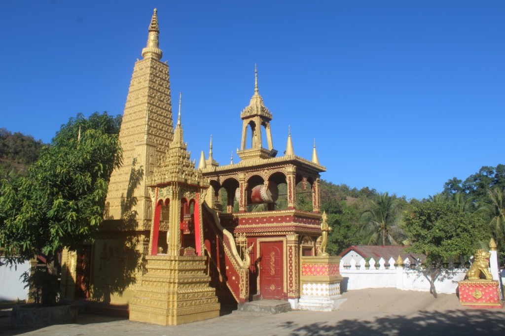 A photograph of golden stupa and drum tower at Wat Naxao Sukharam in Naxao, Laos under vivid blue skies. 