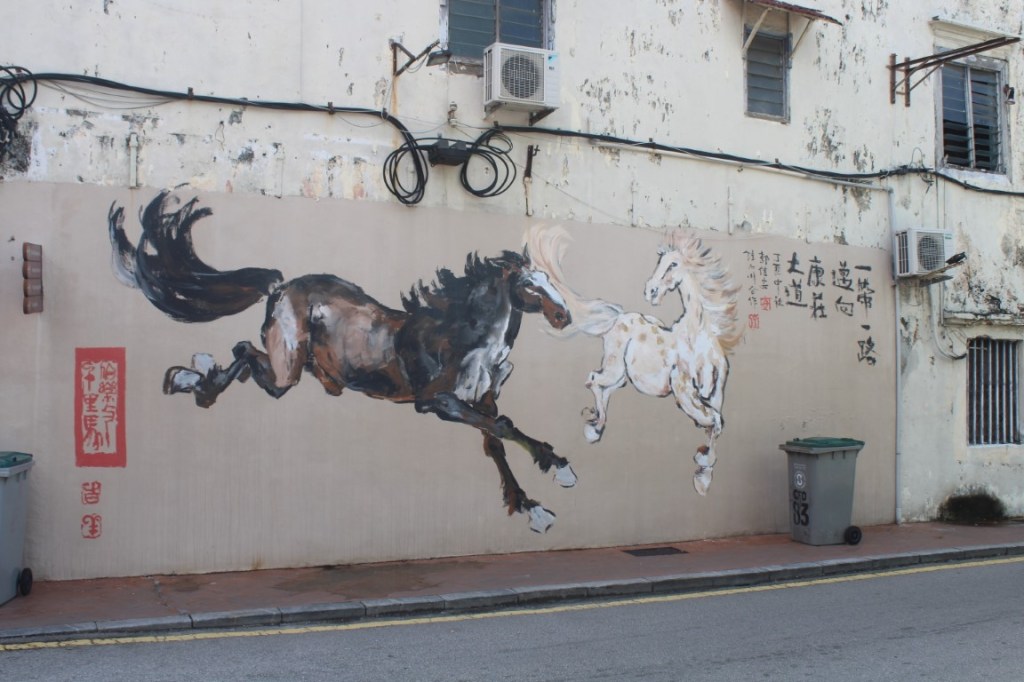 Photo of wall mural of a dark horse and a white horse with Chinese text and stamp. Taken in Melaka, Malaysia's Chinatown [Jonker Street area.]