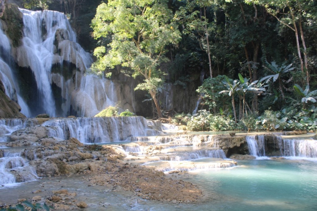 Photograph of rushing water and a teal pool at Kuang Si waterfall in Laos. 