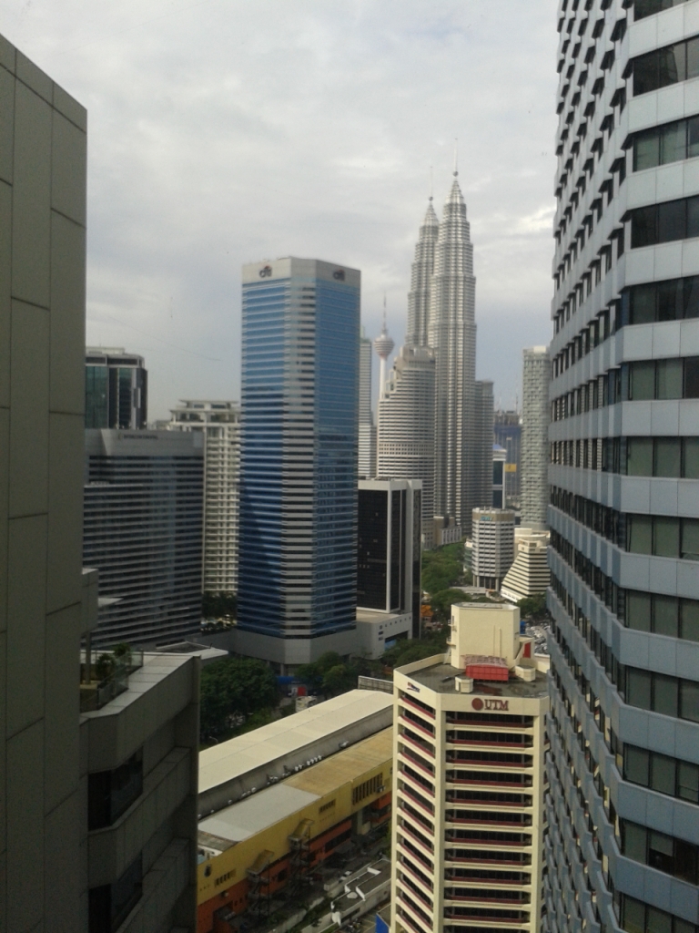 Photograph of Kuala Lumpur's skyscrapers, including the Petronas Towers, taken from a high hotel window. 