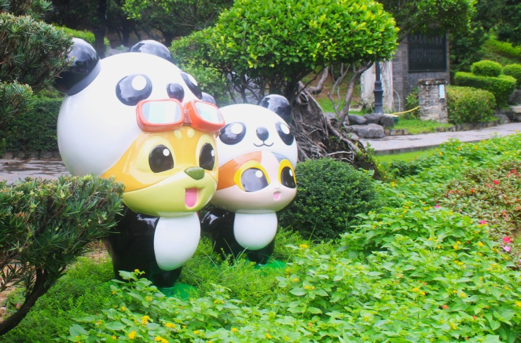Photograph of whimsical statues (chipmunks disguised as pandas) surrounded by greenery in the Kowloon Walled City Park of Hong Kong.  