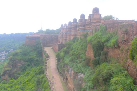 Photograph showing the facade of Gwalior Fort the roadway to the main entrance, and surrounding greenery. Taken from the Gujari Mahal end of the Fort.