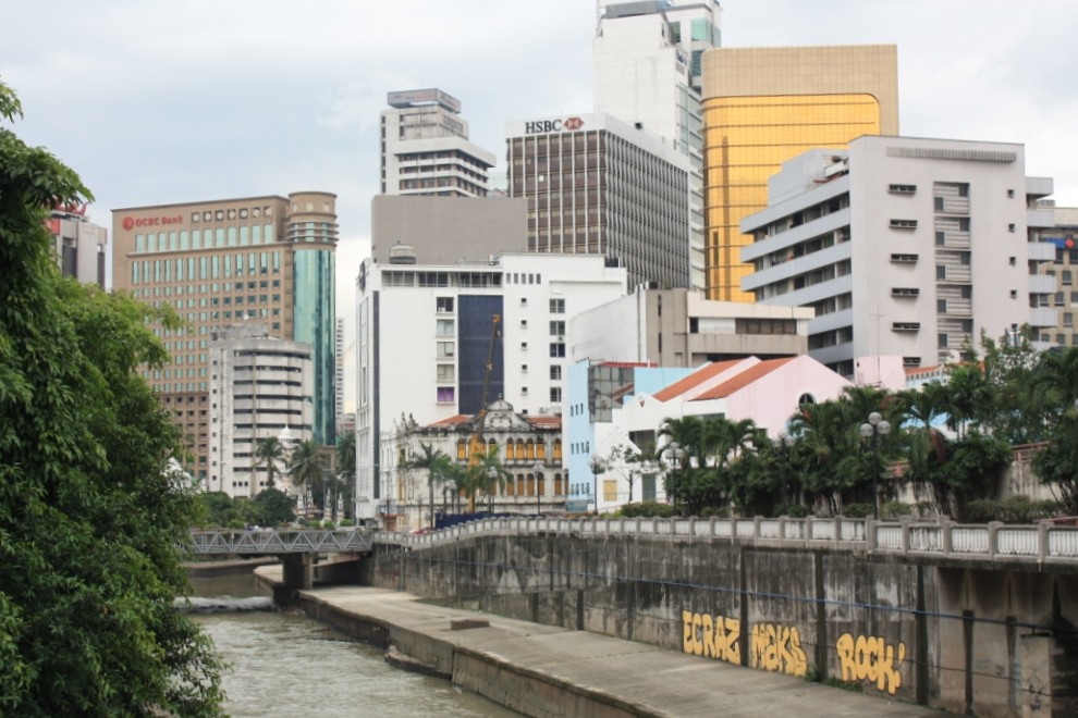 Photograph of a dense cluster of buildings in the heart of Kuala Lumpur, Malaysia. Taken from beside the Klang River.