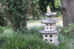 Photograph of a small stone pagoda in the grass at the base of an evergreen tree. Taken in Medellin, Colombia at the Castillo Museum and Gardens.