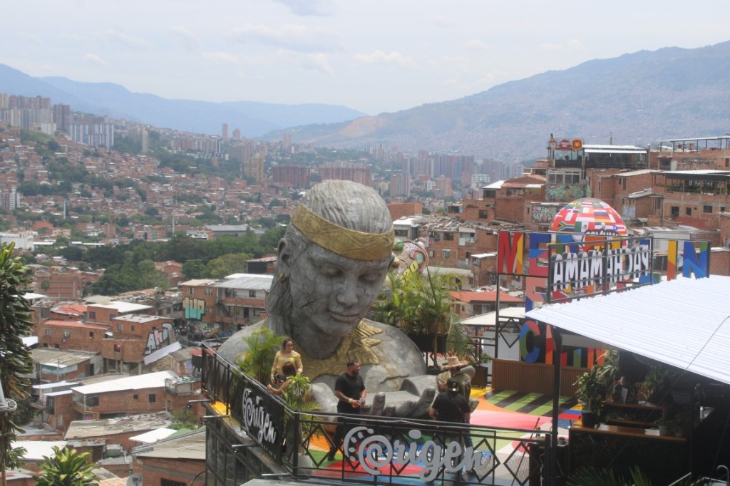 Photograph taken in Comuna 13 featuring large bust sculpture and an overview of part of Medellin.