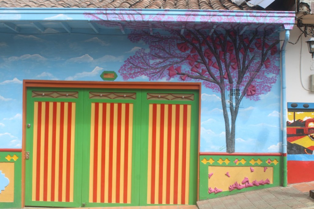 Photograph of a colorful shop front with cherry blossoms and striped doors in Guatapé, Colombia. 