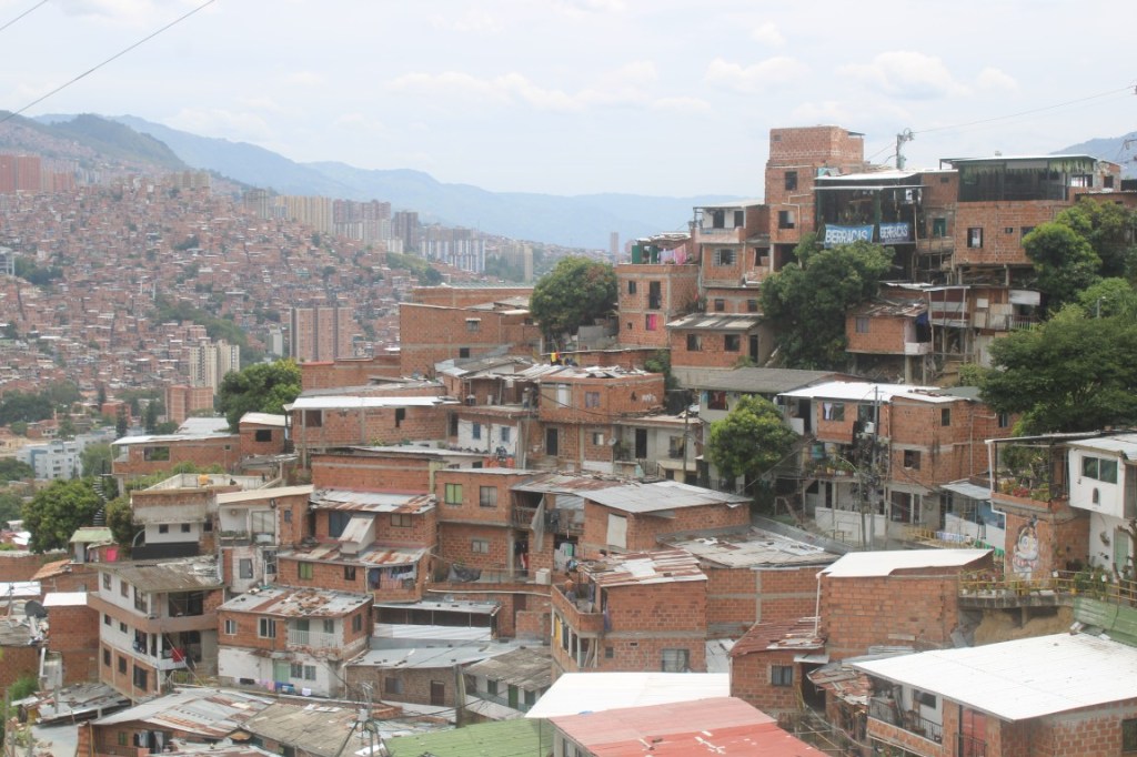 Photograph of a barrio on a hill with city beyond in Medellin, Colombia. 
